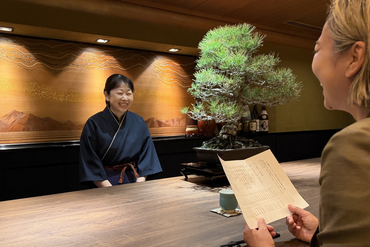 メニューを手にスタッフと会話するカウンター席の女性